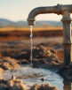 Rusty water pump on land with dry and cracked soil.