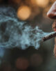 Close up of a man smoking a marijuana cigarette with smoke coming out of his mouth.  Room for text