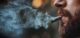 Close up of a man smoking a marijuana cigarette with smoke coming out of his mouth.  Room for text